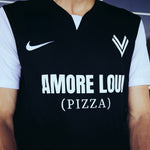 Mann trägt schwarzes ASK Voitsberg Trikot mit weißem kurzen Ärmeln mit weißem ASK Voitsberg Wappen auf der linken Brustseite, weißem Nike Swoosh auf der rechten Brustseite und Amore Loui (Pizza) Logo in weiß über die gesamte Brust.