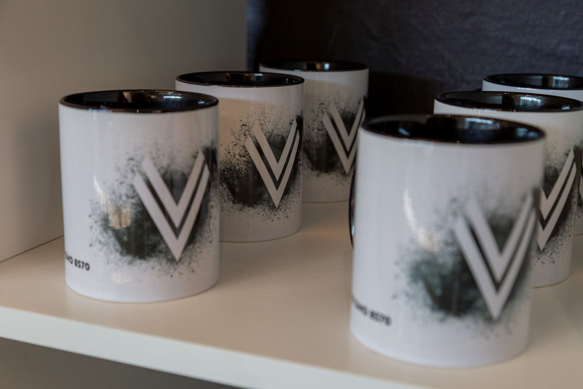Mehrere weiße Tassen mit V Kohle Design des ASK Voitsberg im Regal