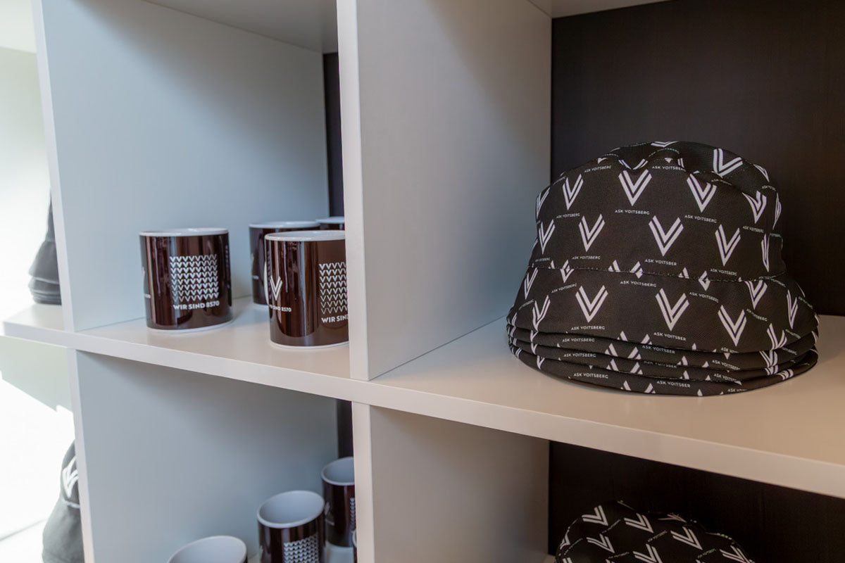 Präsentation der ASK Voitsberg Sonnenhüte und Tassen im weißen Regal im ASK Voitsberg Store