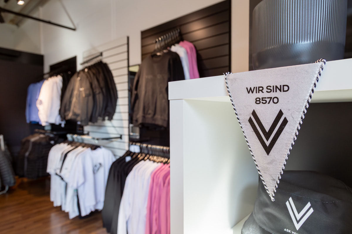 Detailansicht von ASK Voitsberg Wimpel in weiß und diversen Pullovern und Jacken im Hintergrund