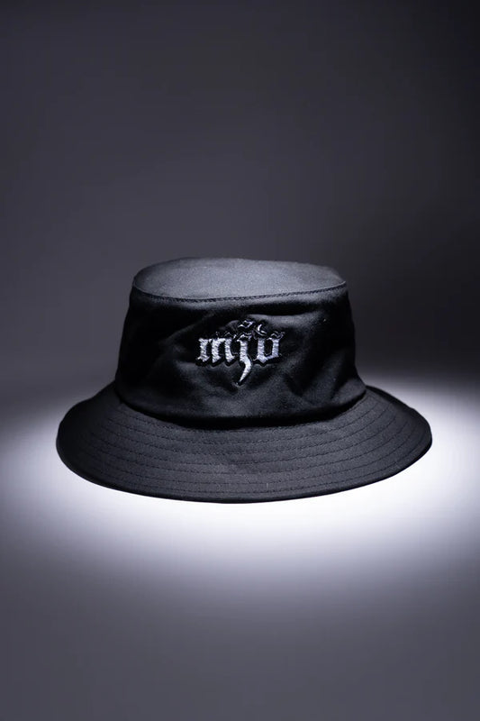 Schwarzer Sonnenhut mit 'MJV' Logo in weiß. Bucket Hat vor grauem Hintergrund von oben beleuchtet.