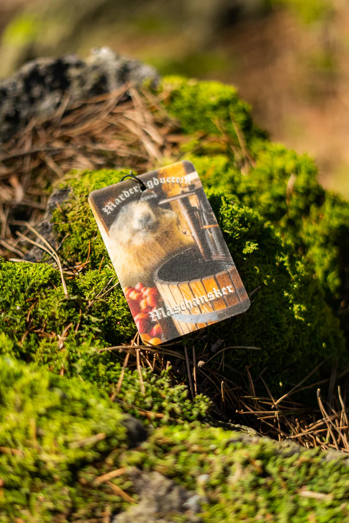 Duftbam 'Maschansker' Vorderseite auf bemoostem Stein. MJV Logo in weiß und Marder vor Mostpresse. 'Maschansker' Duftbaum vom Marderjagdverein.