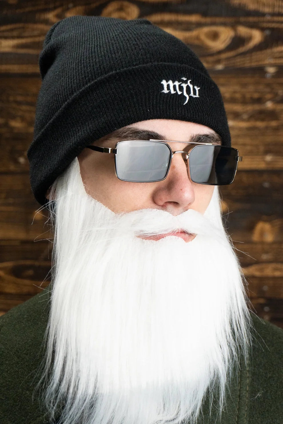 Mann trägt eine schwarz Sonnenbrille, eine schwarzer Haube mit gesticktem, weißem Marderjagdverein Logo, weißen langen Bart und grüner Jacke.