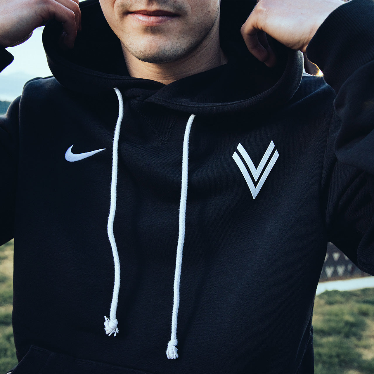 Detailansicht einer Person die einen schwarzen Nike Hoodie mit weißem Nike Swoosh und ASK Voitsberg 3D Wappen trägt.